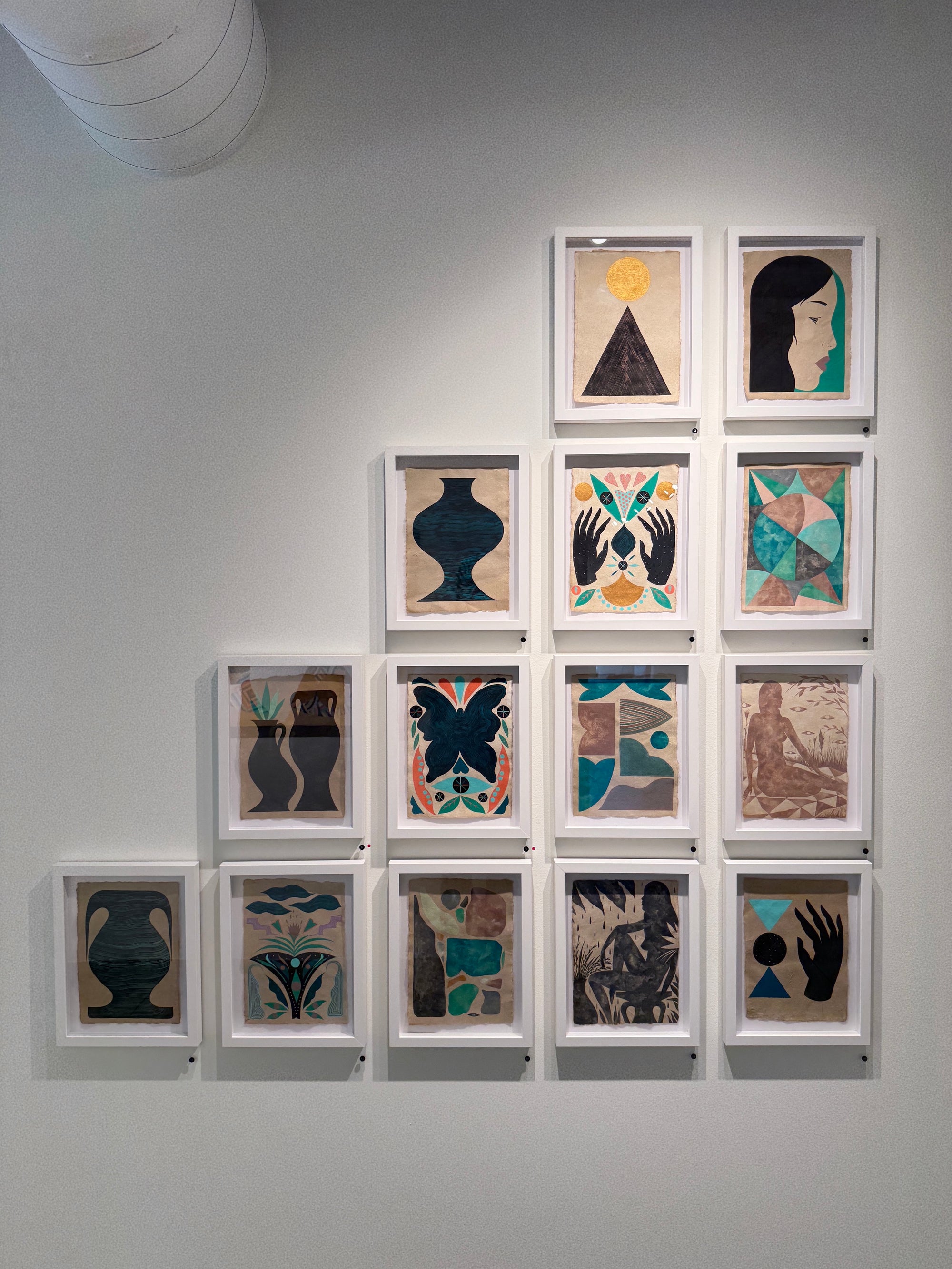 Grid of framed artworks by adrian landon brooks
 on a gray wall